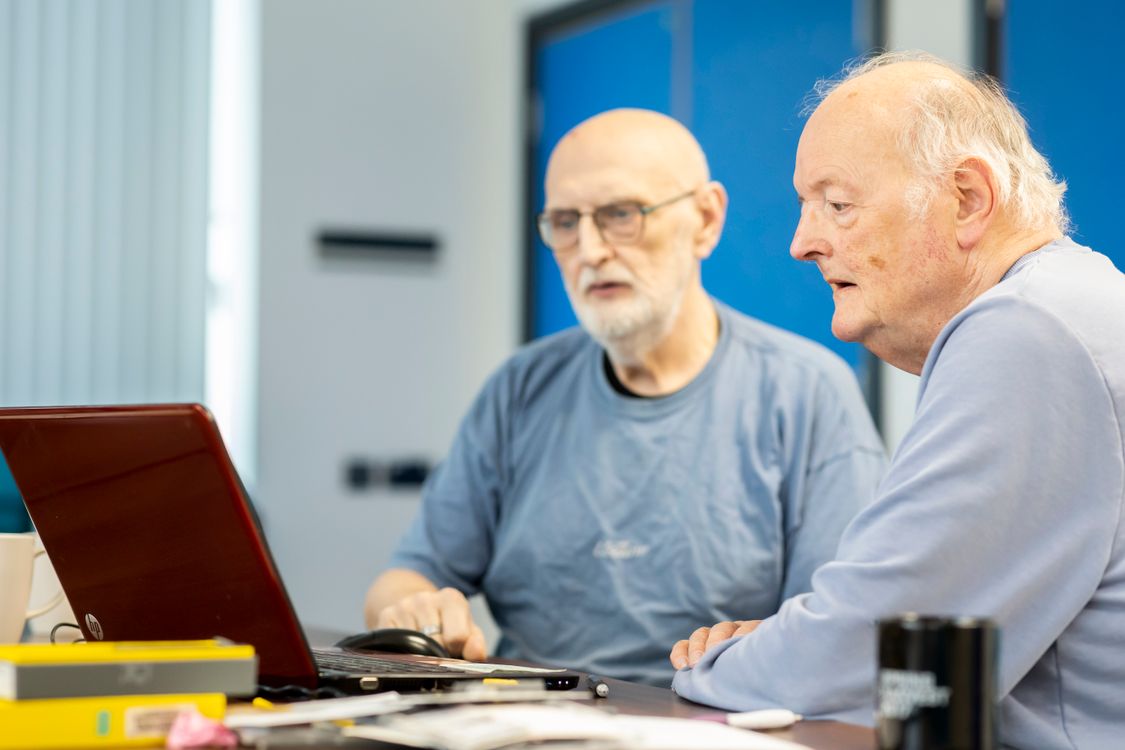 Two older men sitting together and using a laptop at a table.